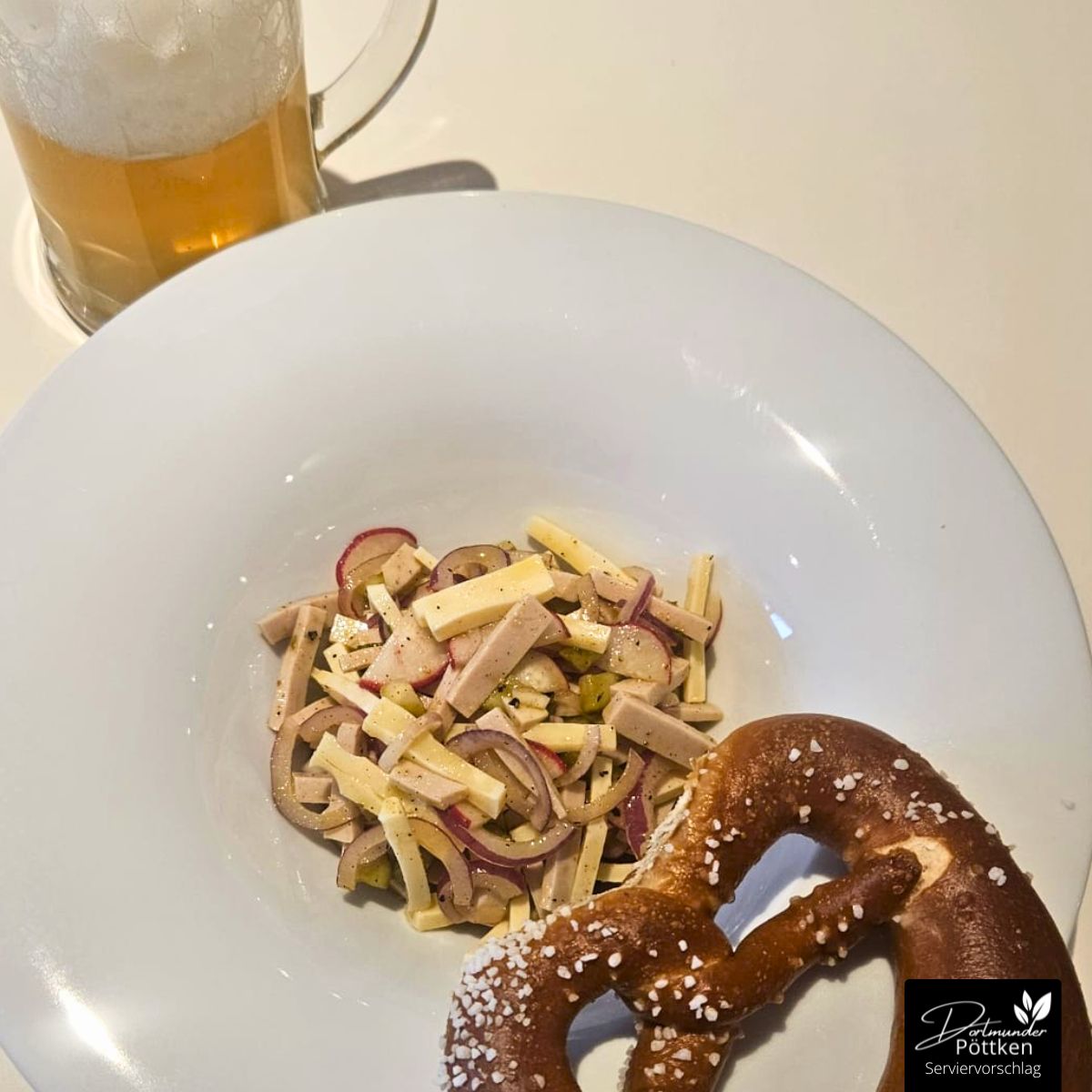 Schweizer Wurstsalat mit Emmentaler, Lyoner, roten Zwiebeln, Radieschen und Gurken, serviert mit Brezel und Bierglas.