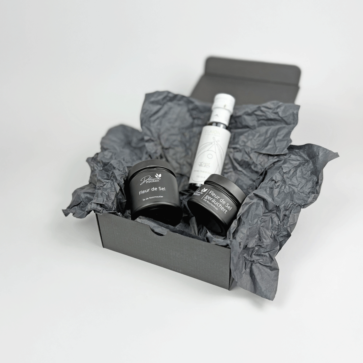 Offene Geschenkbox mit Fleur de Sel geraeuchert_ Fleur de Sel und Olivenoel auf weissem Hintergrund